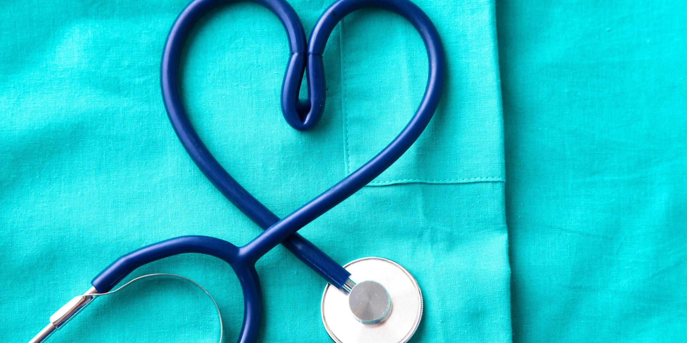 A stethoscope shaping a heart and a clipboard on a medical uniform, closeup.
